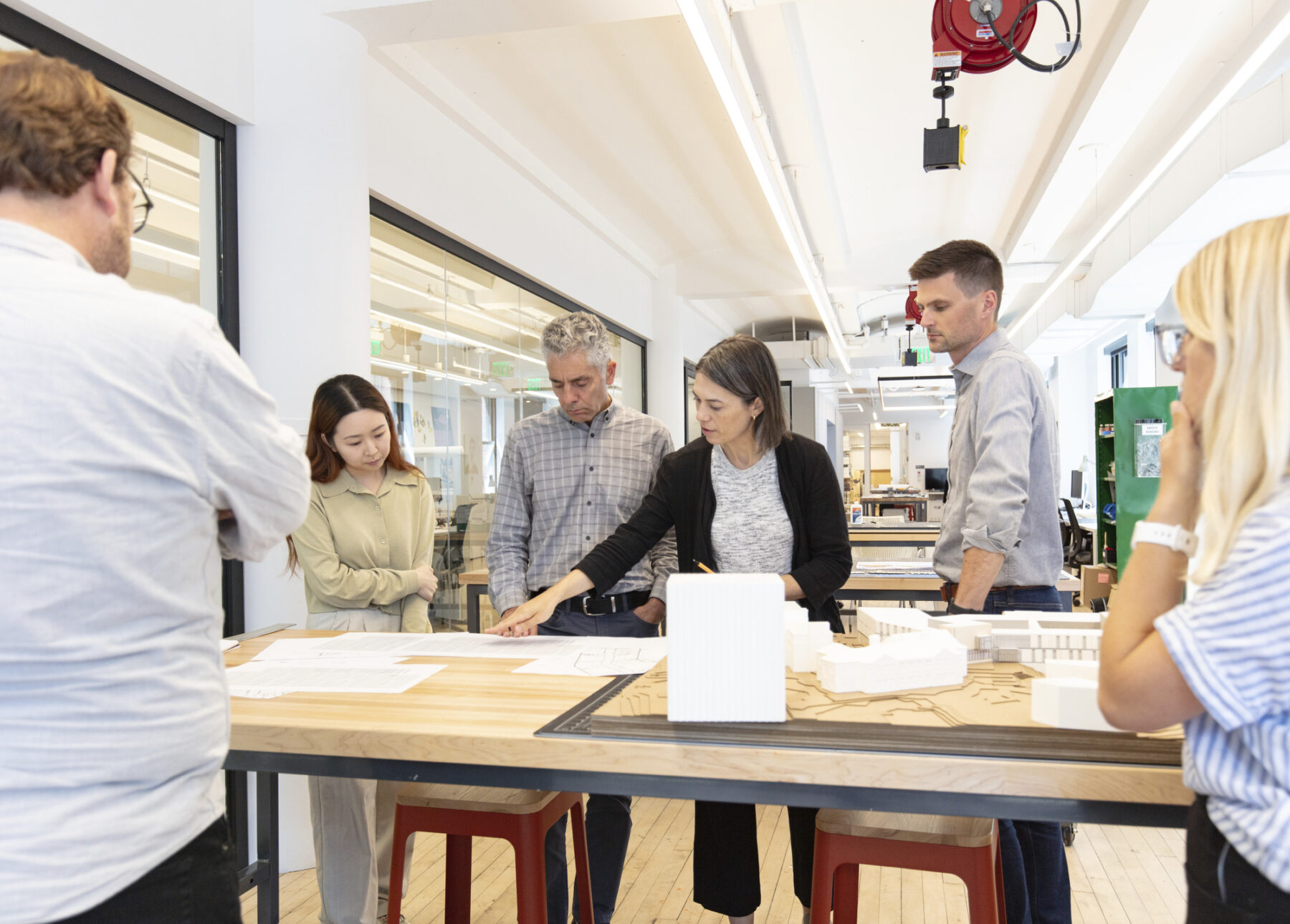 photo of design team surrounding table inside fabrication studio with documents and woman pointing