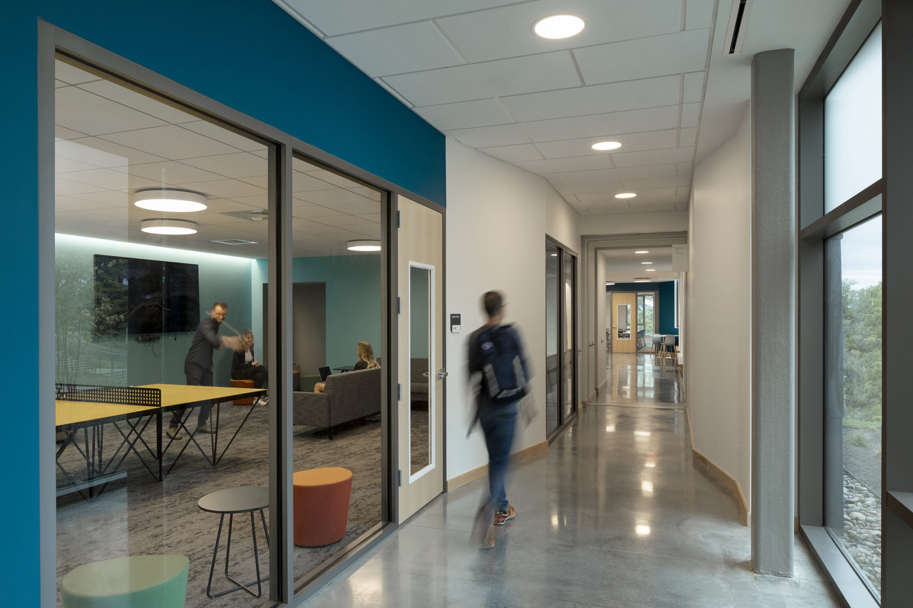 interior photo of student walking down corridor past a rec room with other students playing ping pong