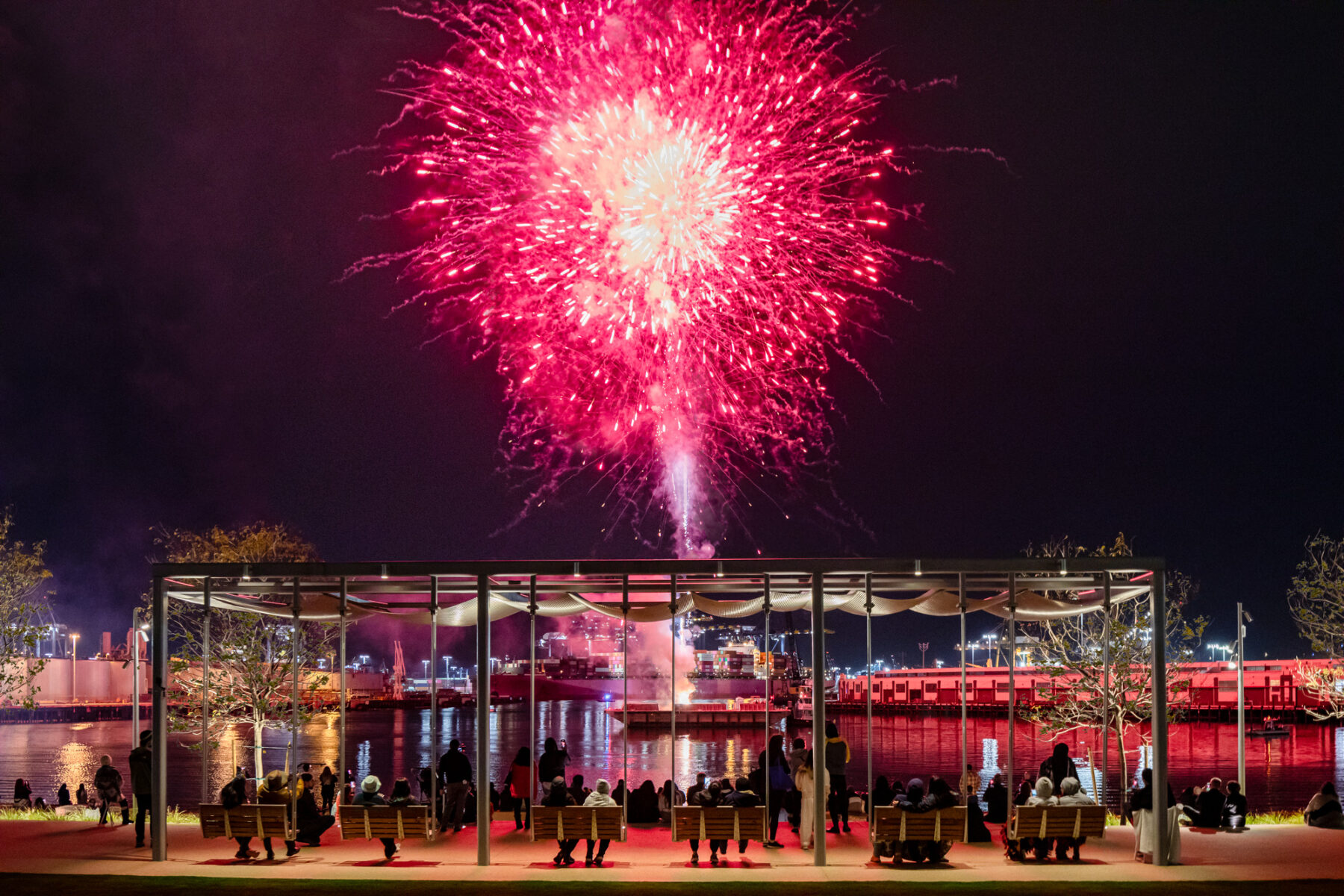 photo of large red firework lighting up the sky as onlookers from the promenade enjoy the spectacle