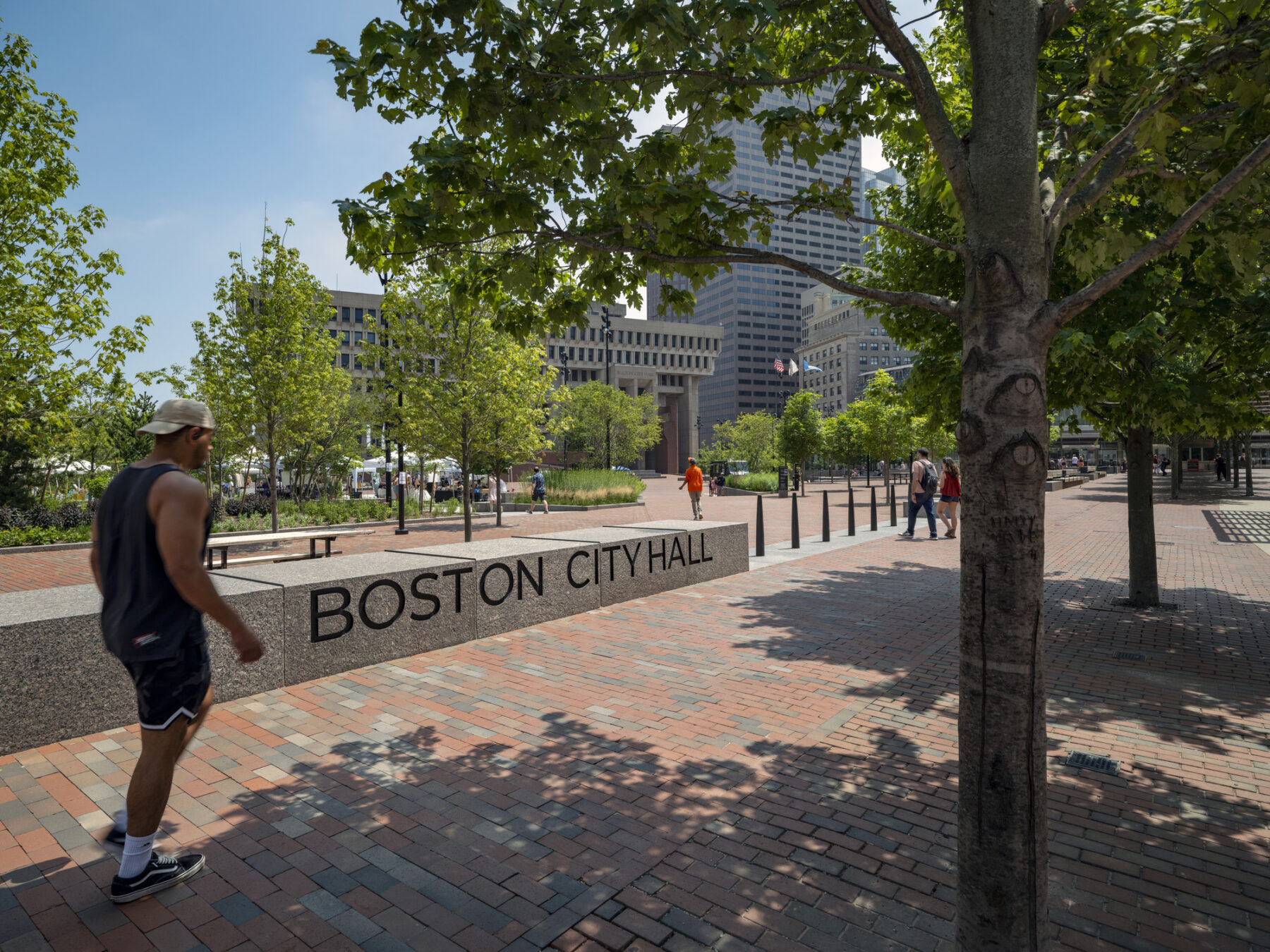 Photo viewing the main plaza and City Hall from Congress Street with trees framing the view and casting shade as pedestrians walk by