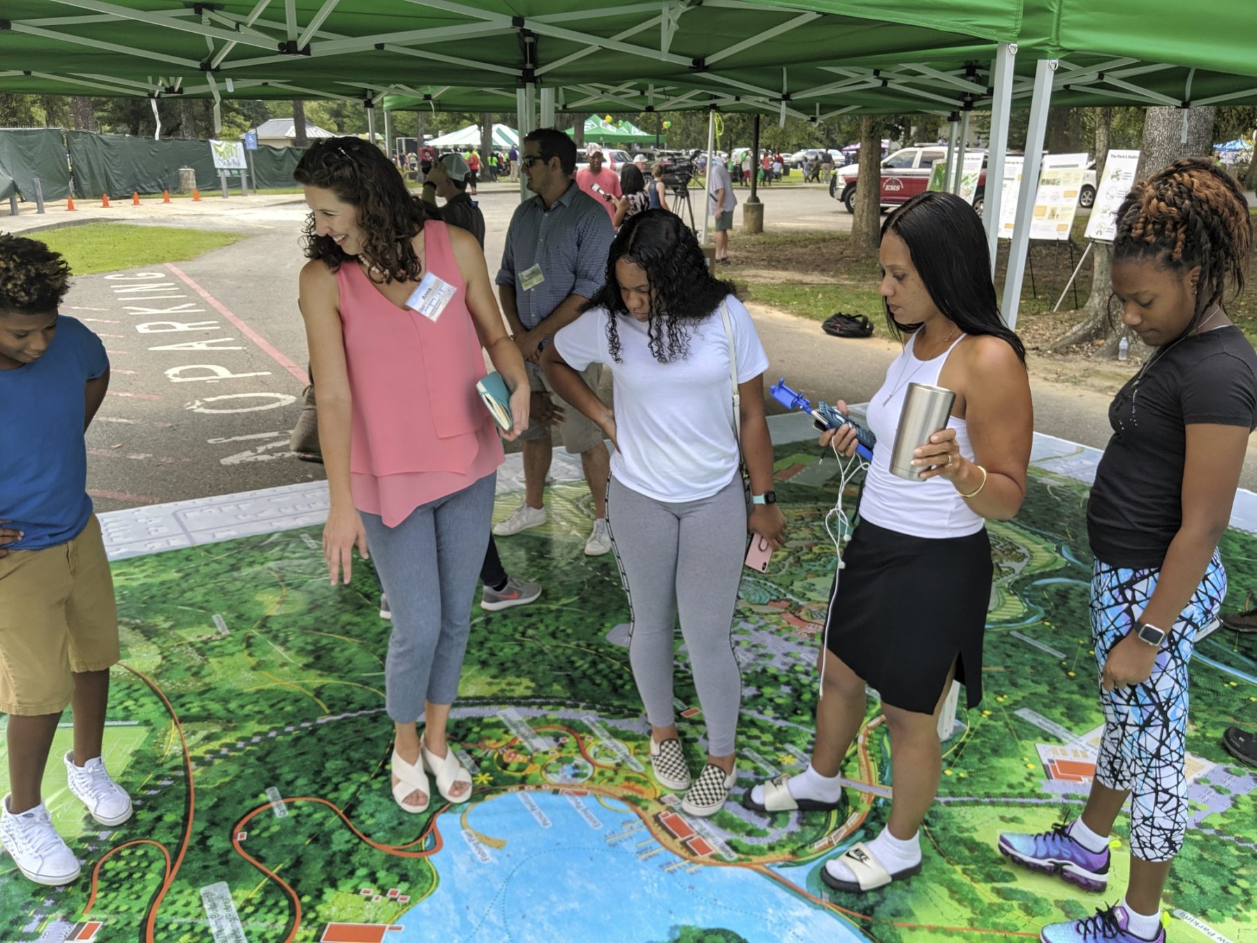 Teens stand on large scale map of Baton Rouge's Greenwood Park site plan, speaking with designer as part of public engagement event