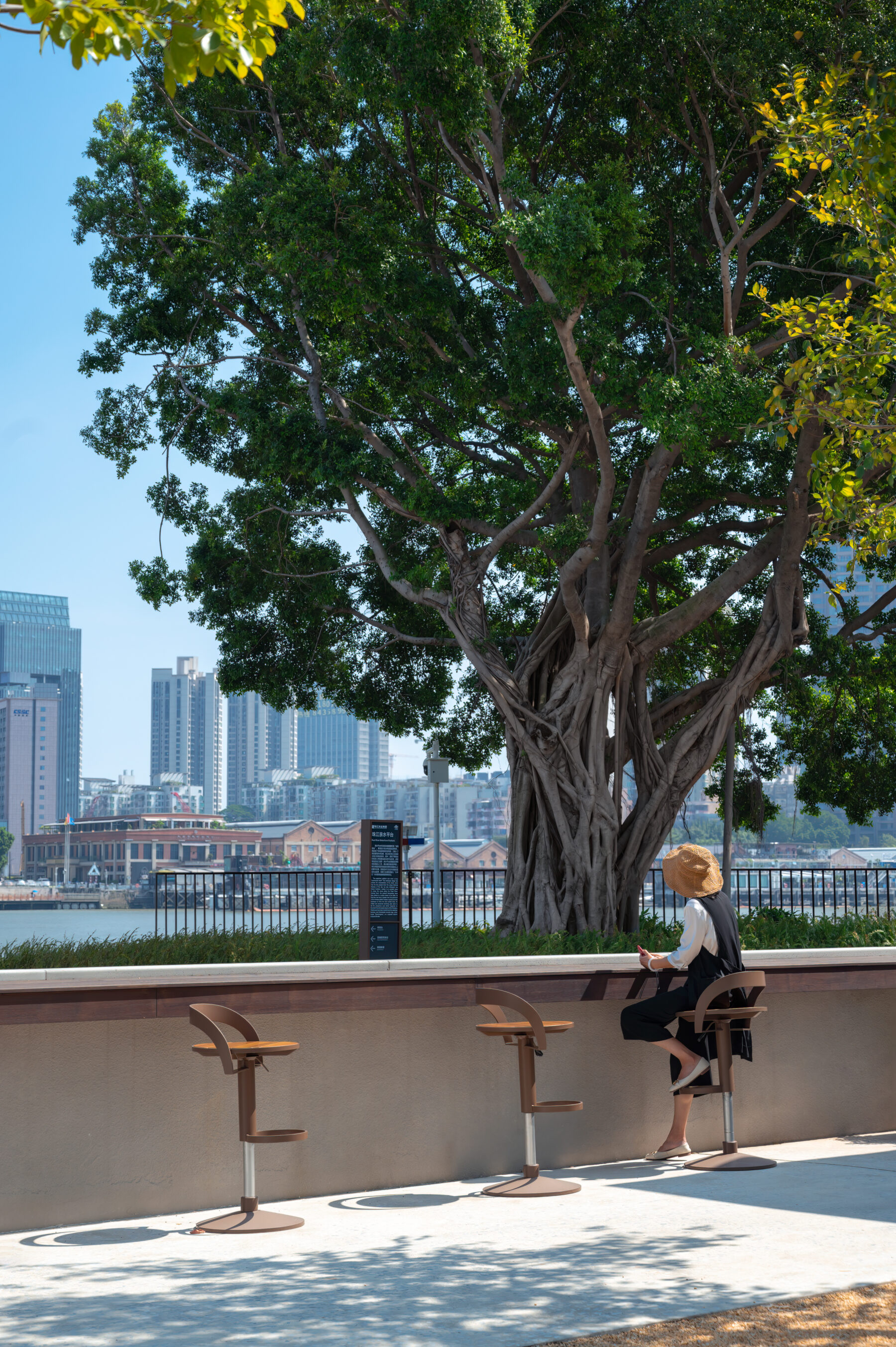 photo of bar seats along the wall parallel to the riverfront with a woman sitting and enjoying the view