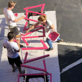 People painting pieces of a chicken coop pink, seen from above