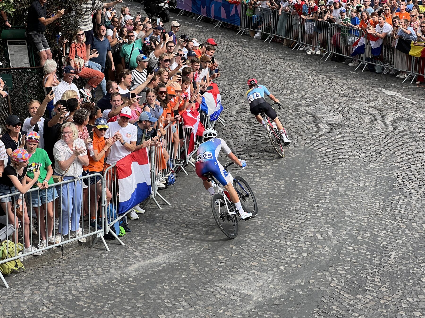 Photo of Olympic cyclists biking over cobblestone streets lined with spectators