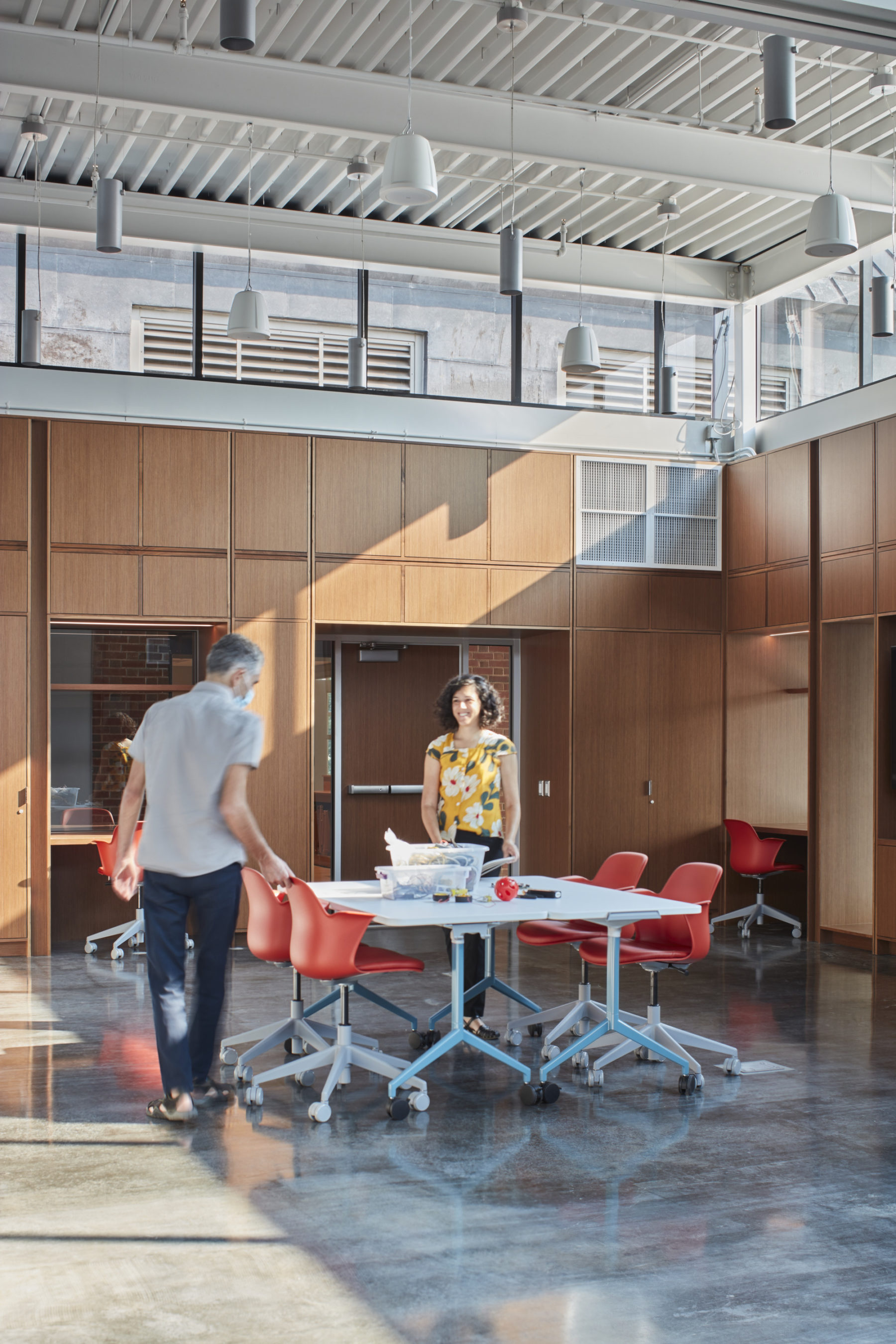 Interior photo of two people standing around a table with orange chairs